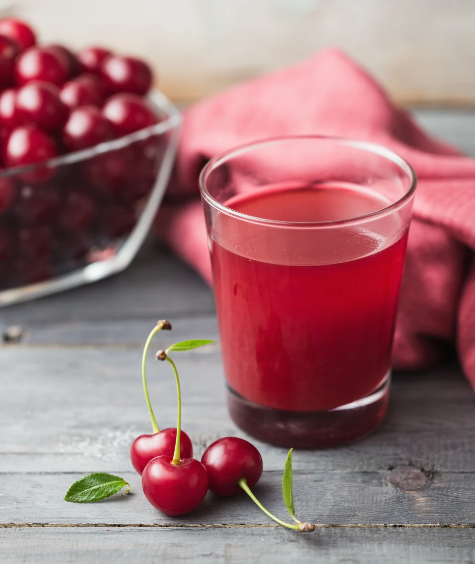 Naturalny sok wiśniowy z Żurawieckich Sadów – tłoczony na zimno, bez cukru Szklanka naturalnego soku wiśniowego Żurawieckie Sady na tle świeżych wiśni