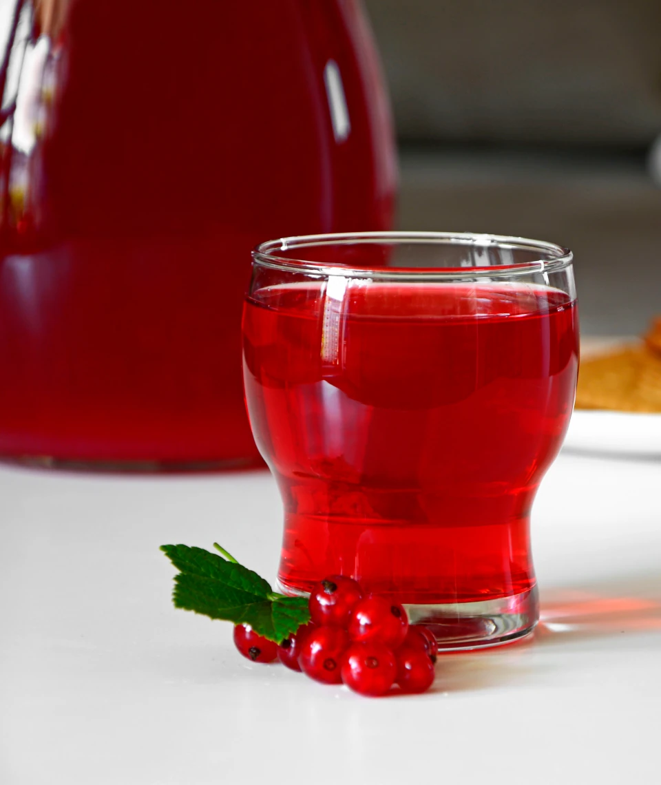 Sok z czerwonych porzeczek Żurawieckie Sady – naturalny smak i rubinowy kolor Szklanka czerwonego soku z porzeczek Żurawieckie Sady, obok świeże owoce z listkiem na białym tle